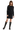 A woman standing wearing a black ribbed mini dress with long sleeves and black boots.